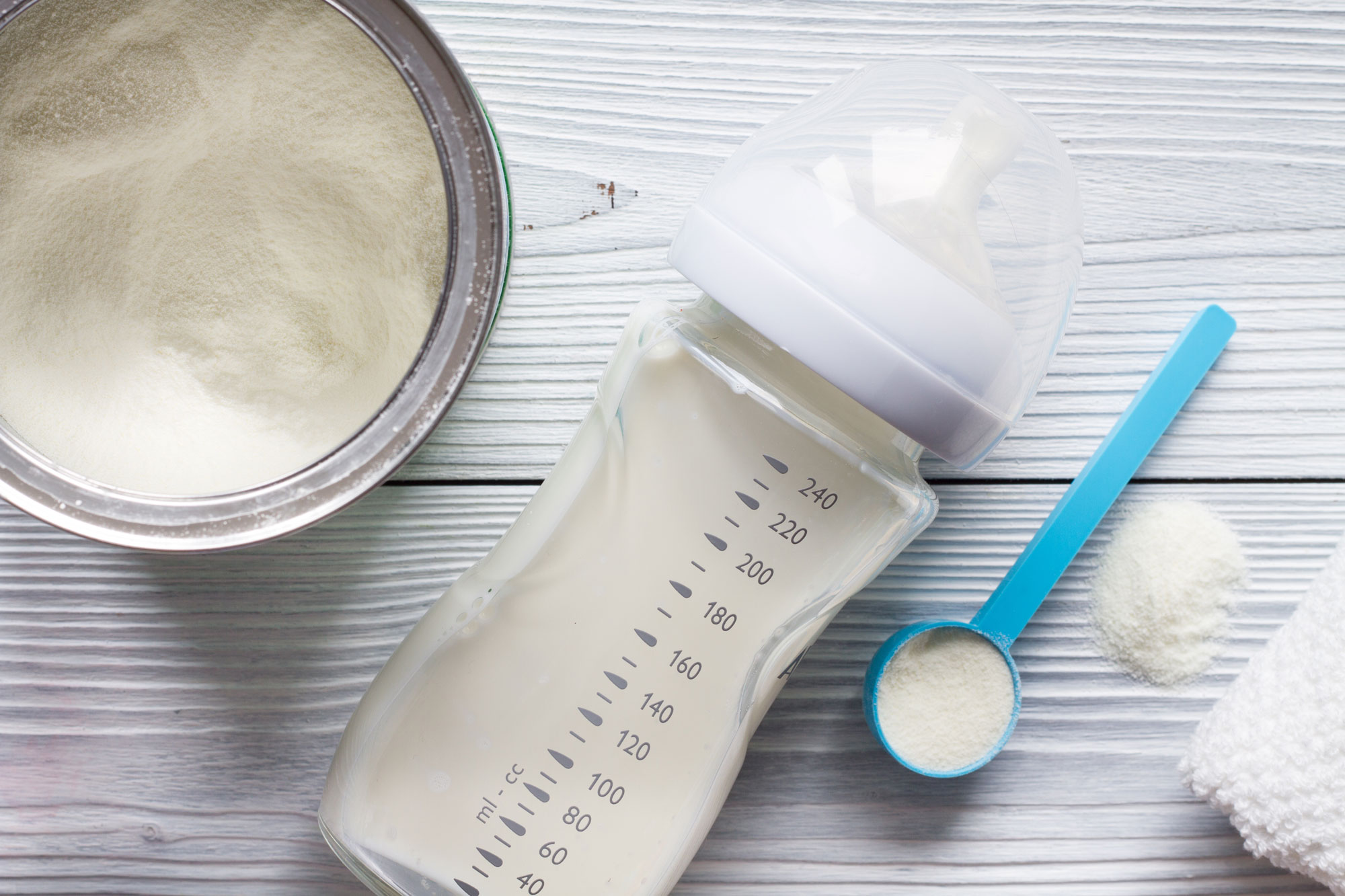 a container of infant formula next to a bottle and scoop